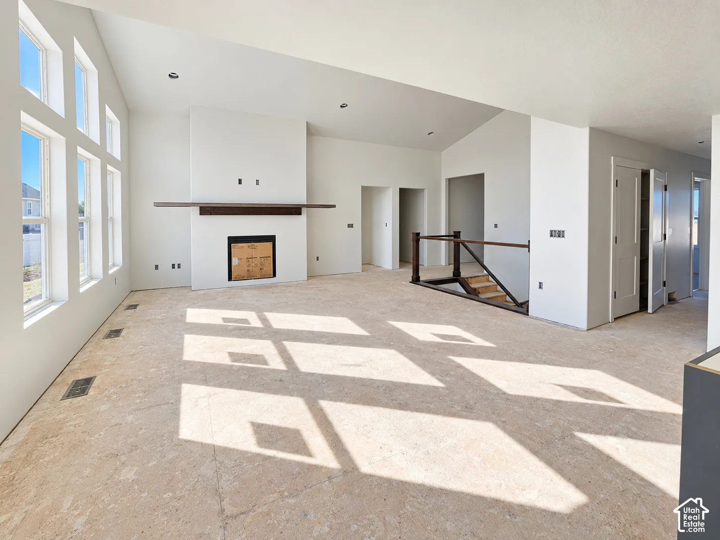 Vaulted ceilings with recessed lighting, floor-to-ceiling windows, a floor-to-ceiling fireplace with a wood mantel, and staircase featuring a metal railing