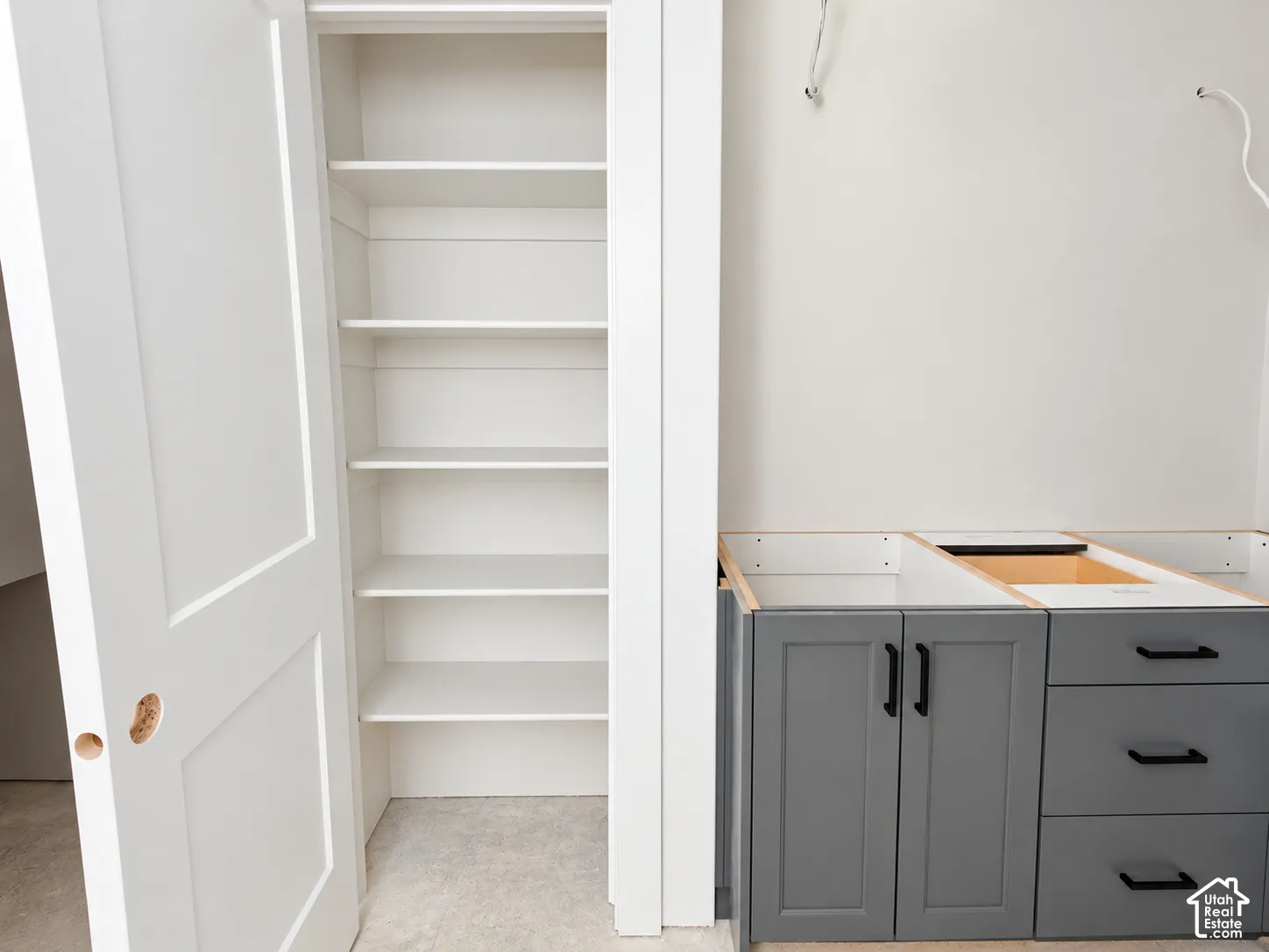 Built-in storage closet with multiple fixed shelves, grey shaker-style base cabinetry, matte black hardware, and drawer unit