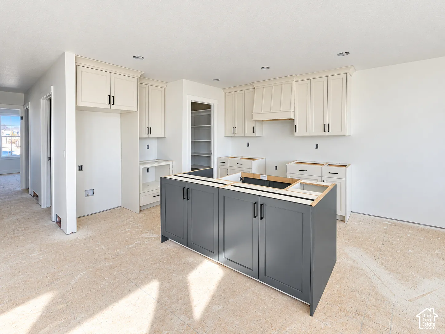 Kitchen featuring cream shaker-style upper cabinetry, a charcoal-toned center island with matte black hardware, custom range hood enclosure, and a walk-in pantry