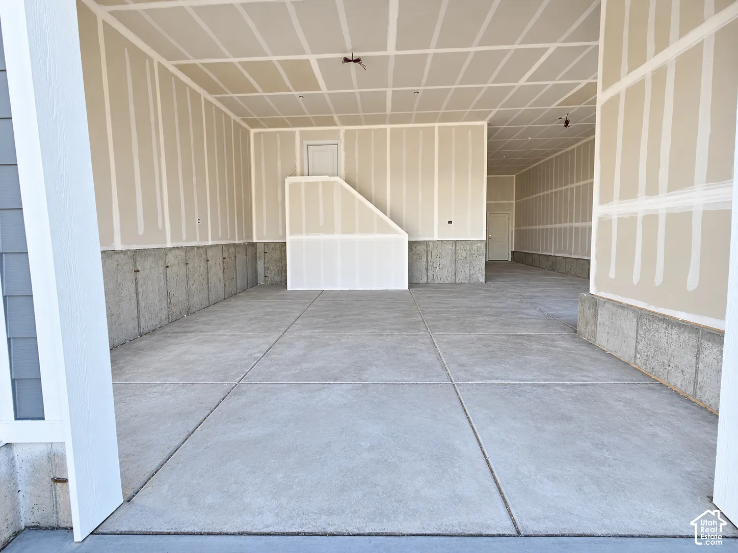 Expansive garage featuring finished drywall, concrete flooring, and exposed concrete foundation walls
