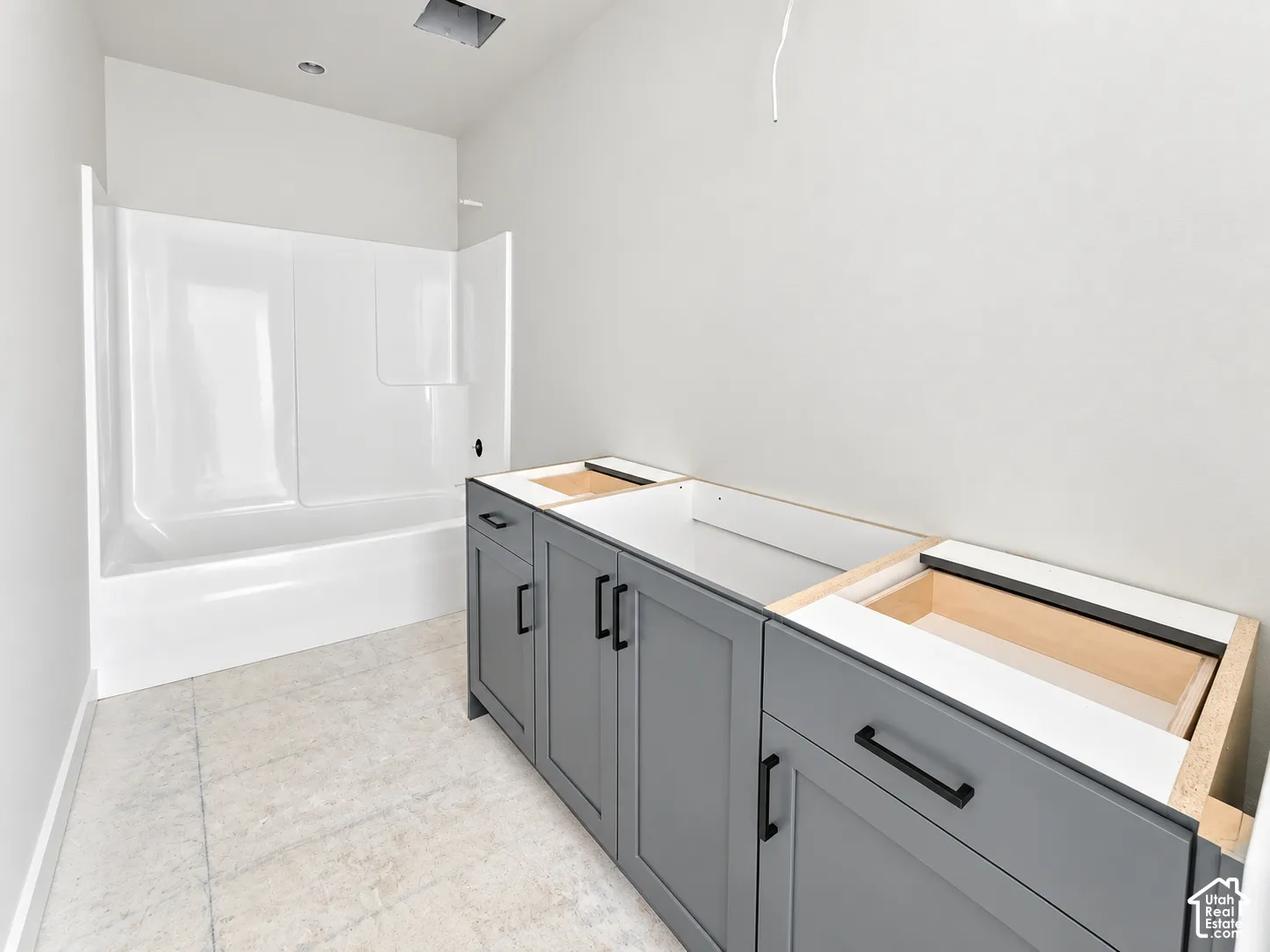 Shaker-style charcoal cabinetry with matte black hardware, white tub-shower surround, and light-toned tile flooring