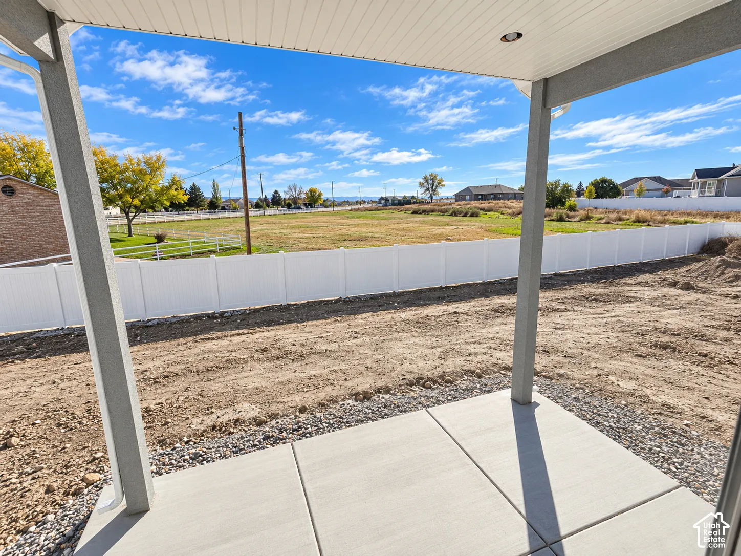 Covered concrete patio with a recessed ceiling light, encompassing a white vinyl privacy fence and open ground
