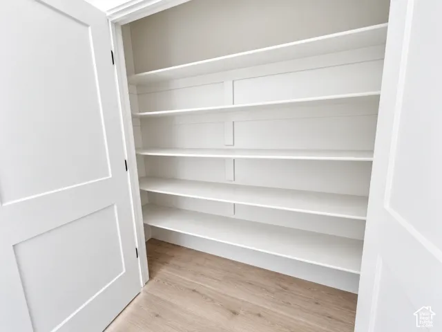 Walk-in storage featuring custom white shelving, shaker-style double doors, and wood-finish flooring