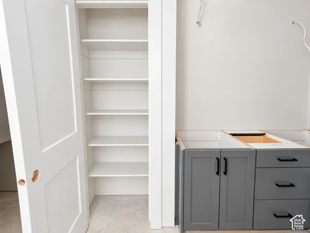 Built-in storage closet with multiple fixed shelves, grey shaker-style base cabinetry, matte black hardware, and drawer unit