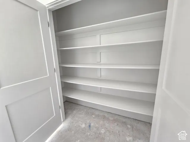 Storage space featuring white shaker-style double doors and four tiers of built-in shelving with vertical bracing