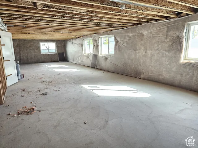 Unfinished space featuring exposed ceiling joists, concrete flooring, four sliding windows, and vapor barrier wall protection