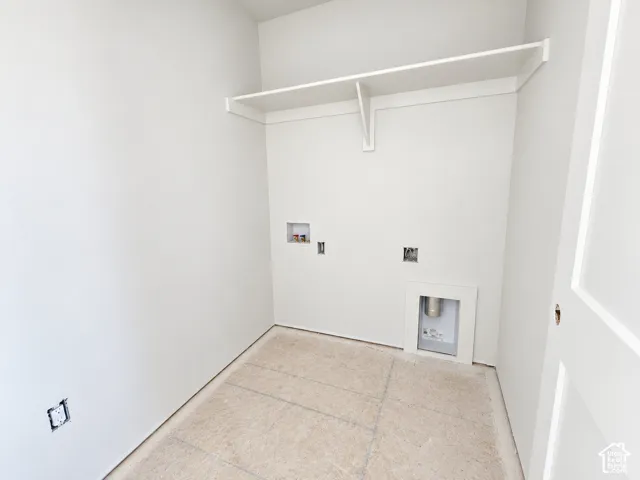 Utility room featuring neutral wall paint, installed upper shelving, and dedicated water and electrical hookups