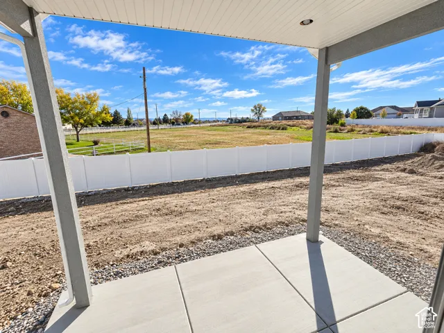 Covered concrete patio with a recessed ceiling light, encompassing a white vinyl privacy fence and open ground