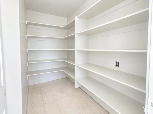 Walk-in pantry featuring expansive L-shaped white shelving and neutral flooring