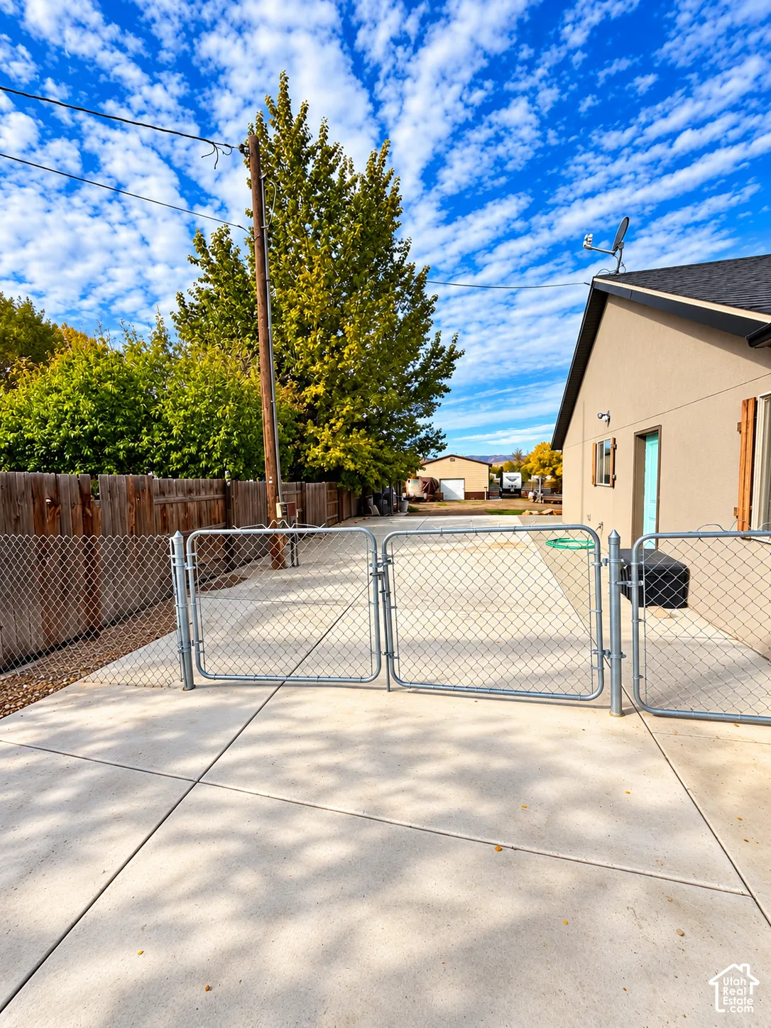 Concrete side parking area enclosed by a metal chain-link gate and a vertical wood privacy fence