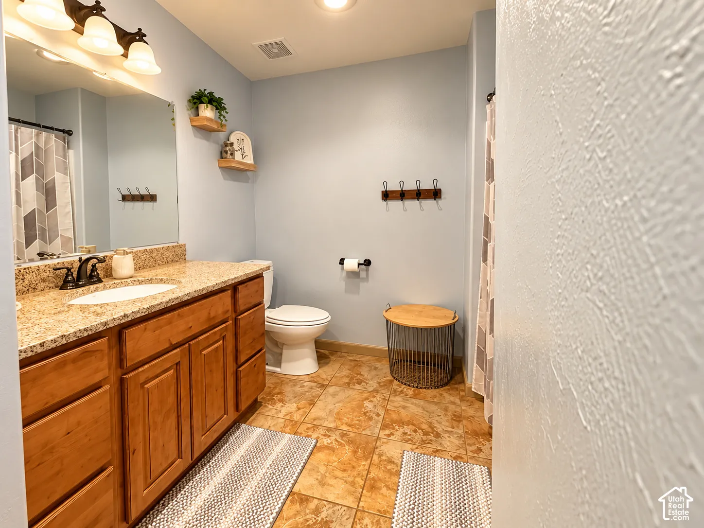 Bathroom featuring a vanity with stone-finish countertop, undermount oval sink, wood-finish cabinetry, tile flooring, and wall-mounted light fixtures