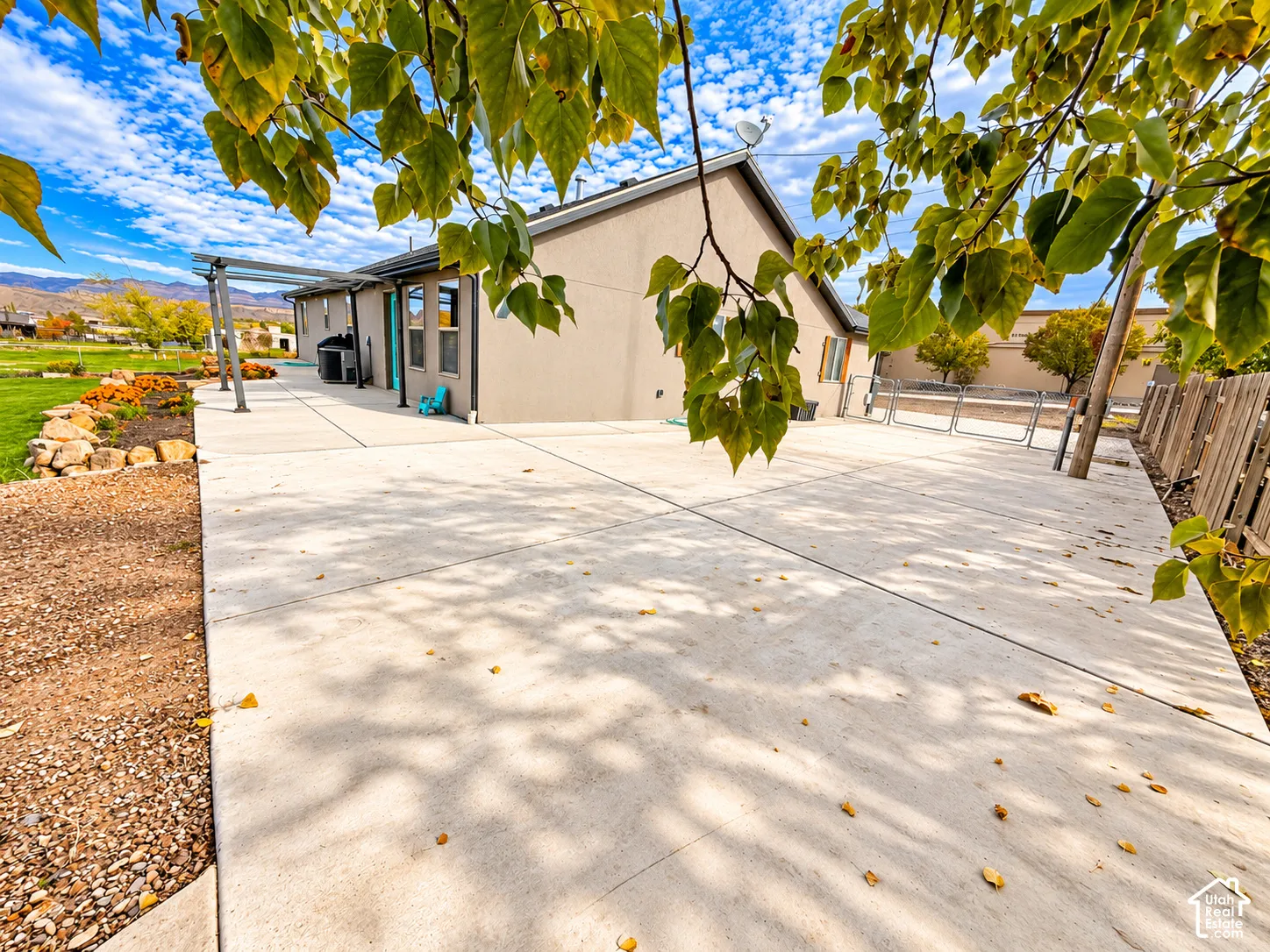 Expansive concrete patio featuring a metal pergola, natural stone landscaping, and a wood-slat privacy fence