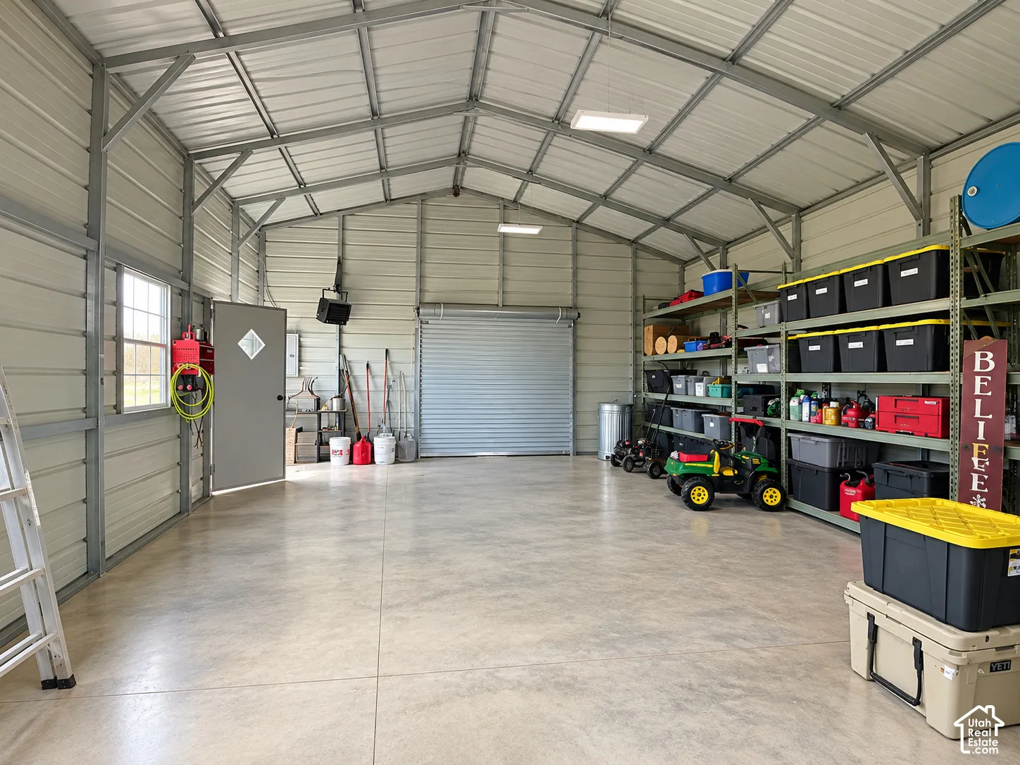 Detached metal workshop featuring a concrete floor, high vaulted ceiling, roll-up garage door, pedestrian door, and grid-panel window