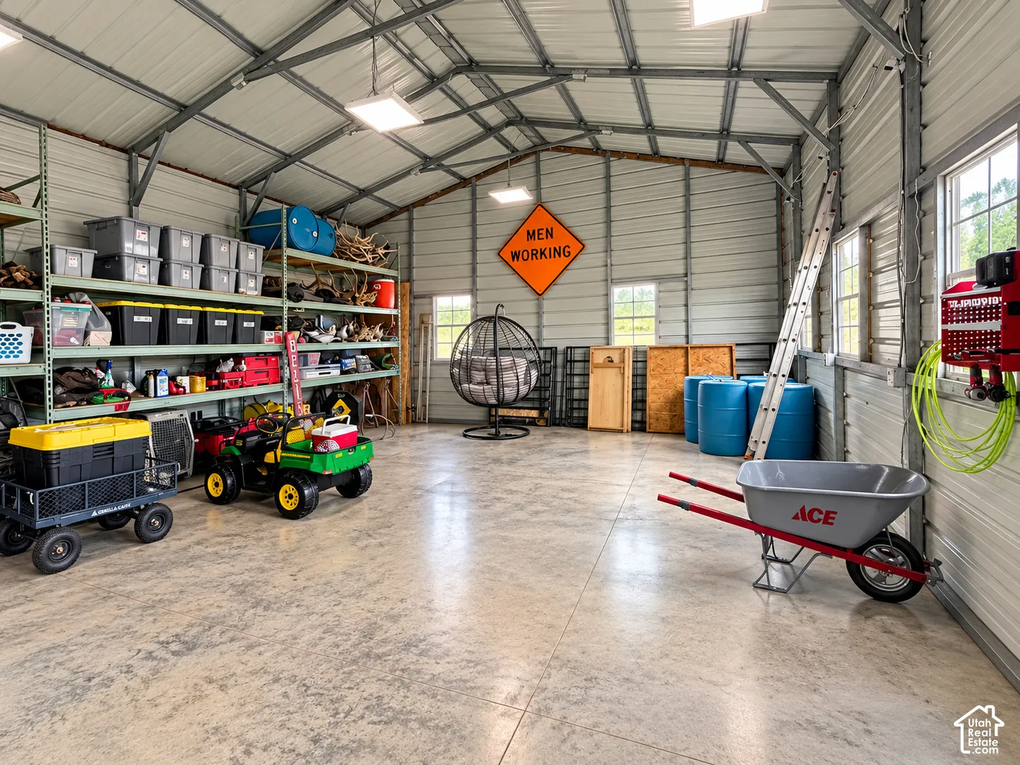 Expansive workshop featuring a concrete floor, metal-paneled walls and ceiling, high-clearance vaulted roofline, integrated shelving units, and multiple windows