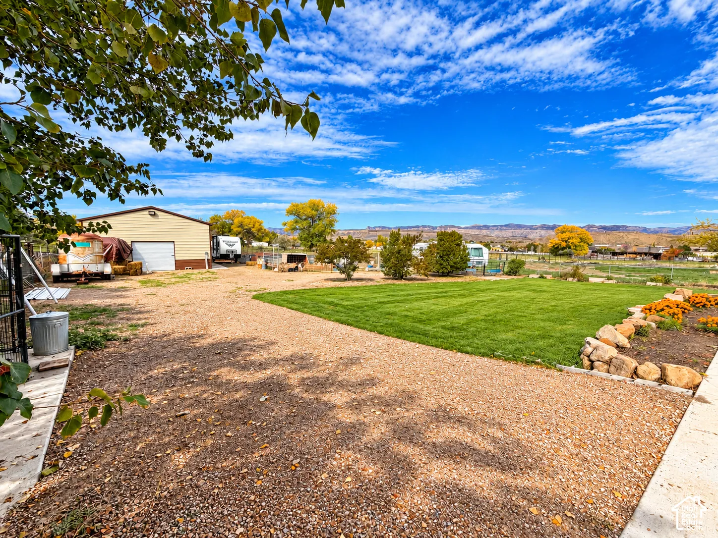 Expansive lot featuring a manicured lawn, stone-bordered garden beds, a detached garage, and gravel surface area