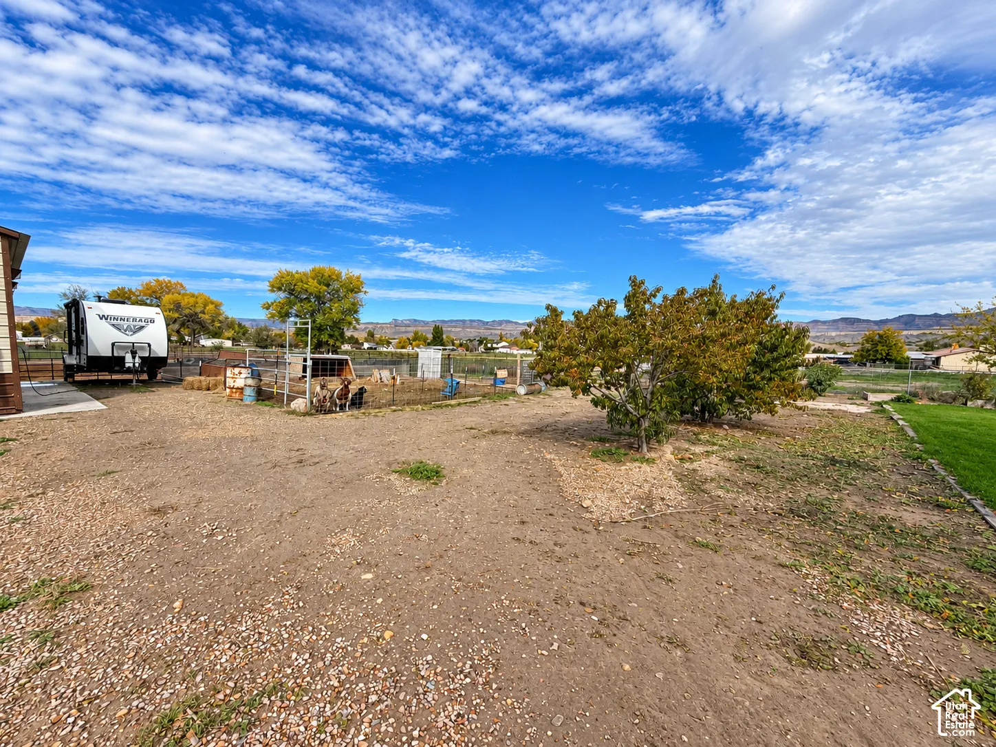 Expansive outdoor space featuring gravel ground cover, fenced enclosure, mature trees, and mountain backdrop