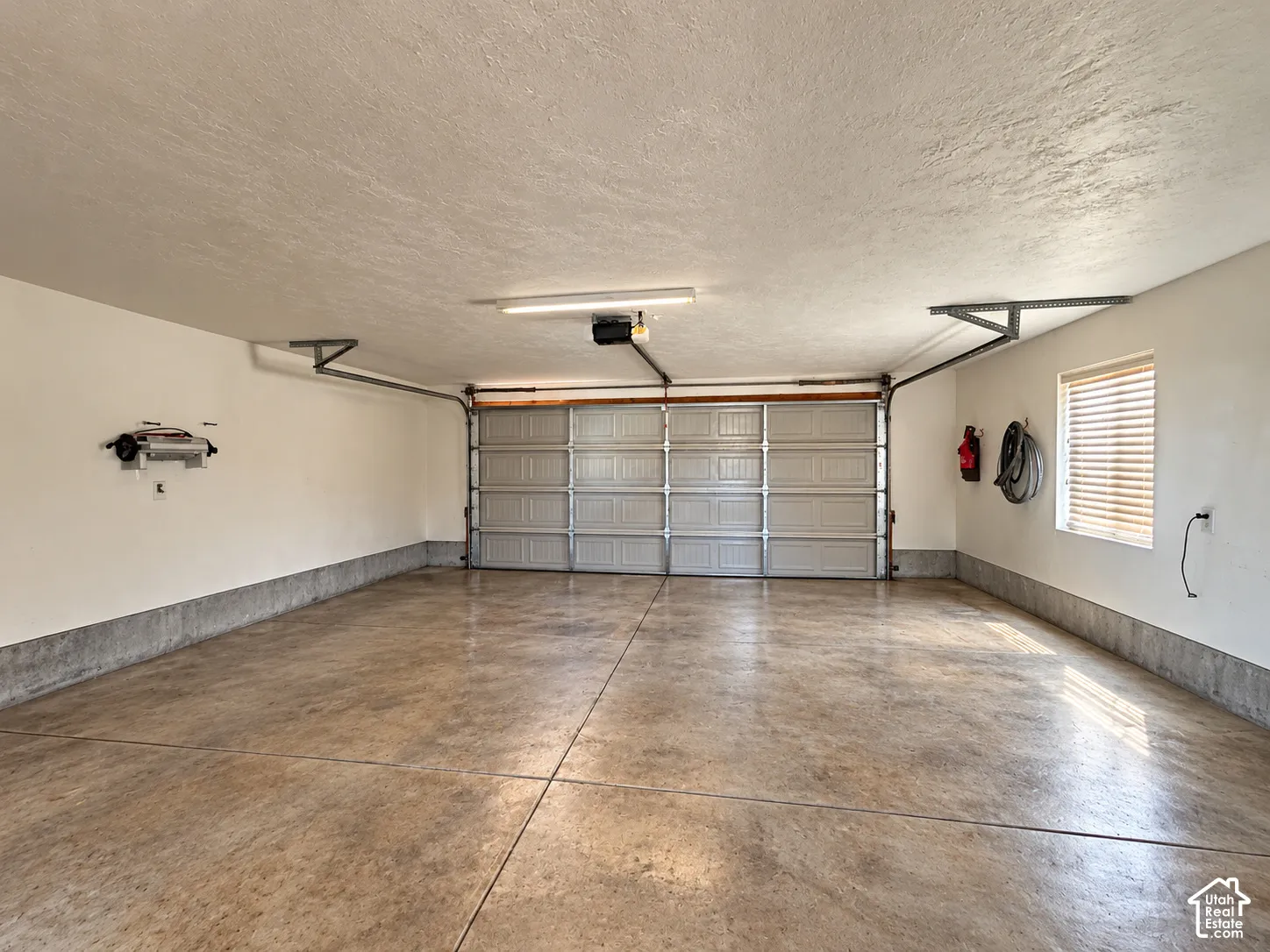 Multi-car garage featuring a concrete floor, painted walls, overhead lighting, and a window with blinds