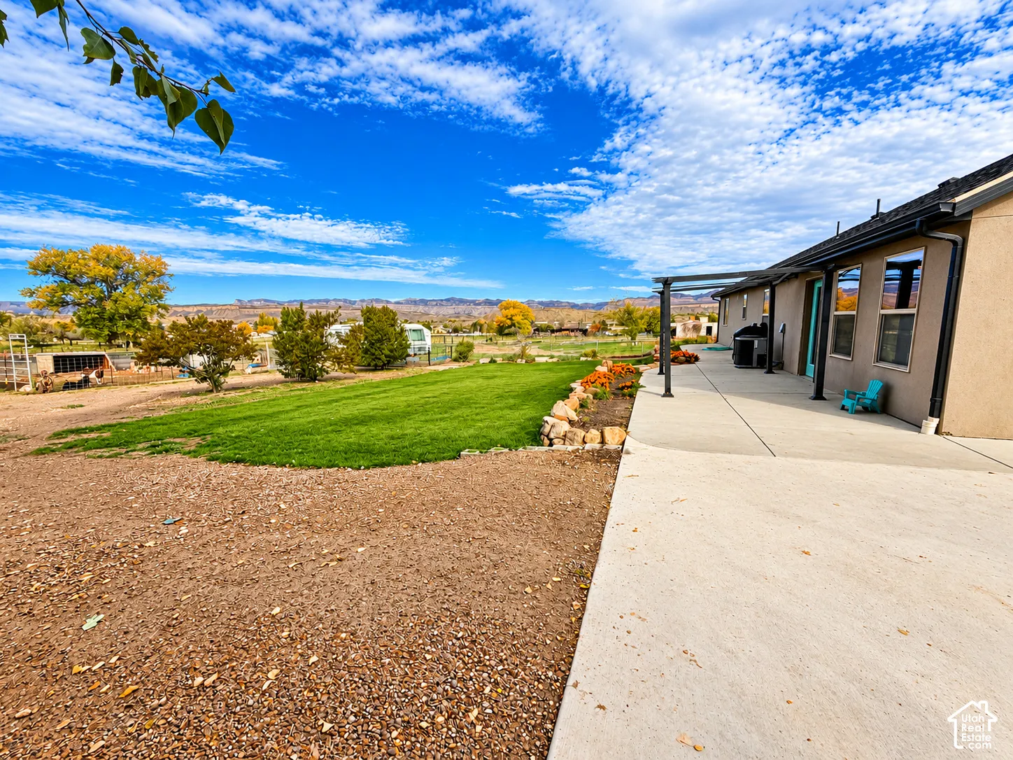 Expansive exterior grounds featuring a covered concrete patio, manicured lawn, natural rock landscaping, and distant mountain topography