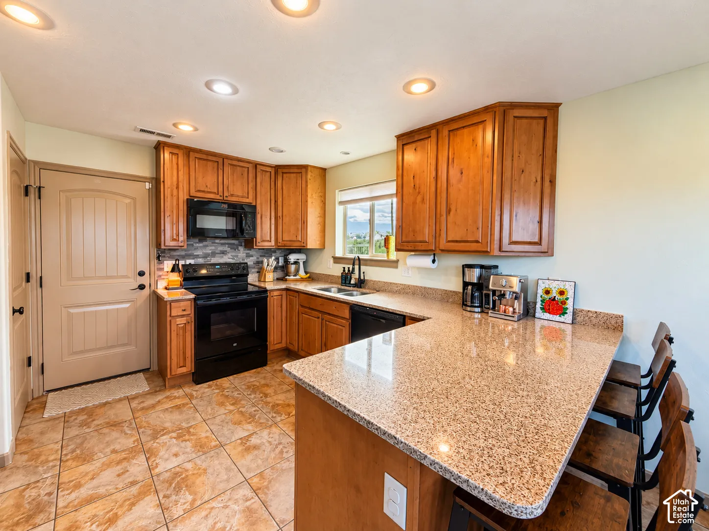 Kitchen featuring natural wood cabinetry, granite countertops, tile flooring, recessed lighting, and a stone-style tile backsplash