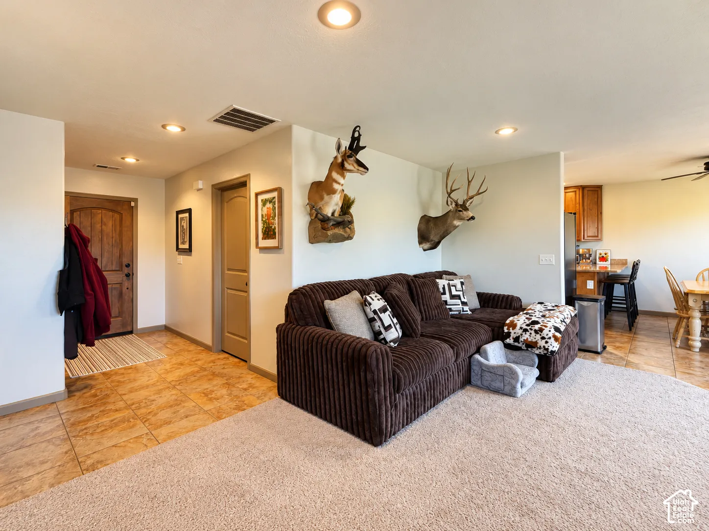 Neutral-tone interior space featuring recessed lighting, square tile flooring, neutral carpeting, and a solid-core wood entry door