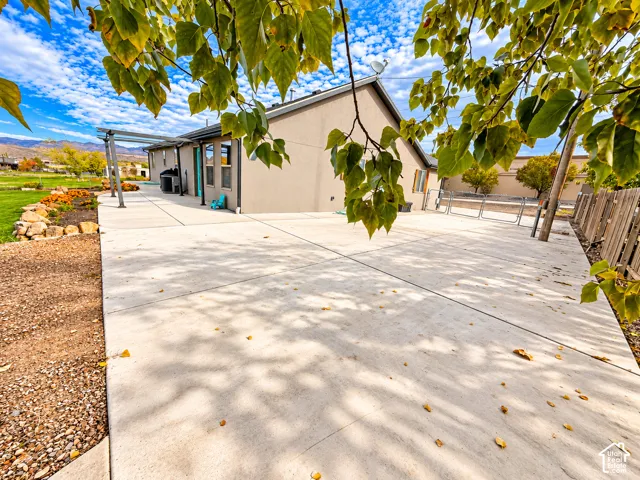 Expansive concrete patio featuring a metal pergola, natural stone landscaping, and a wood-slat privacy fence