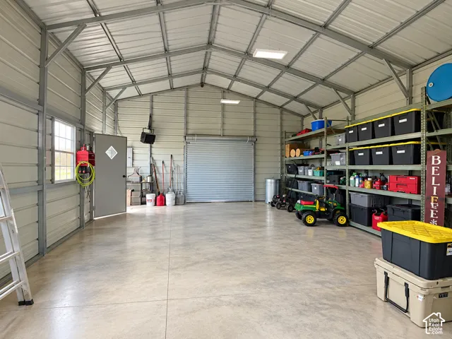 Detached metal workshop featuring a concrete floor, high vaulted ceiling, roll-up garage door, pedestrian door, and grid-panel window