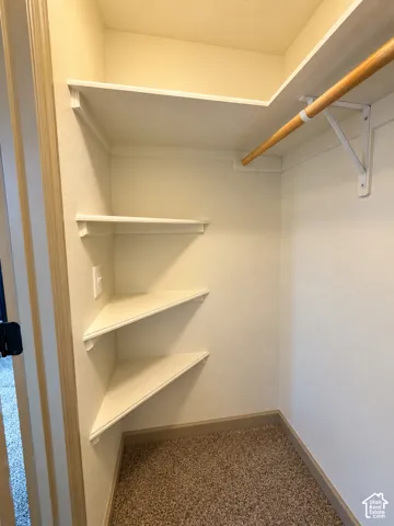 Storage closet featuring built-in corner shelving, a fixed overhead shelf, and a wooden hanging rod