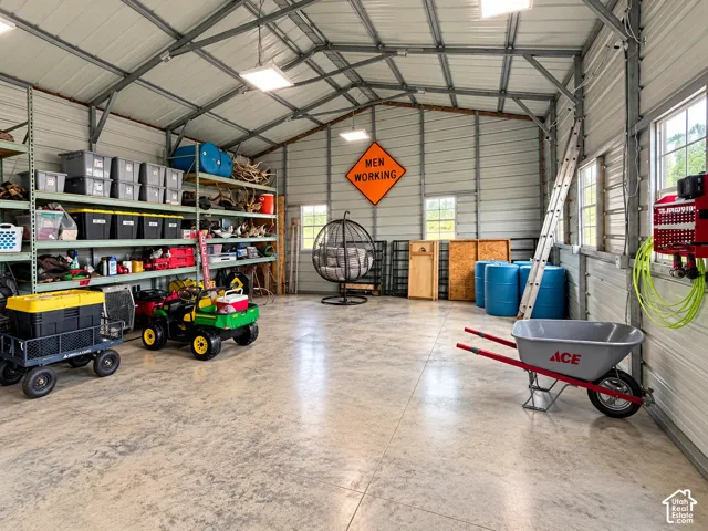 Expansive workshop featuring a concrete floor, metal-paneled walls and ceiling, high-clearance vaulted roofline, integrated shelving units, and multiple windows