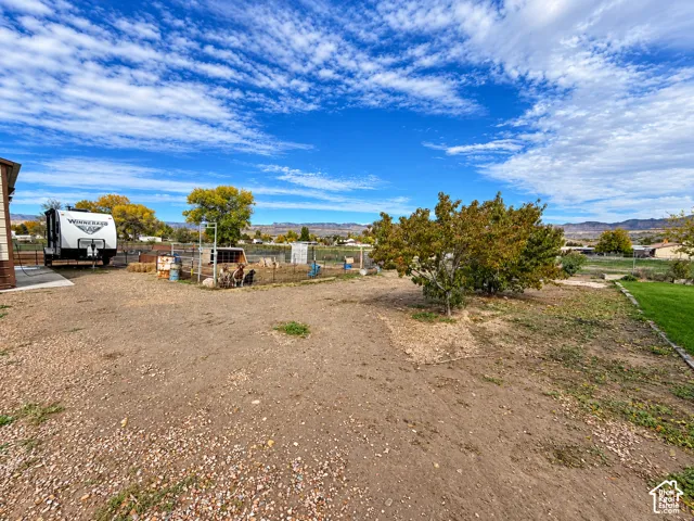 Expansive outdoor space featuring gravel ground cover, fenced enclosure, mature trees, and mountain backdrop