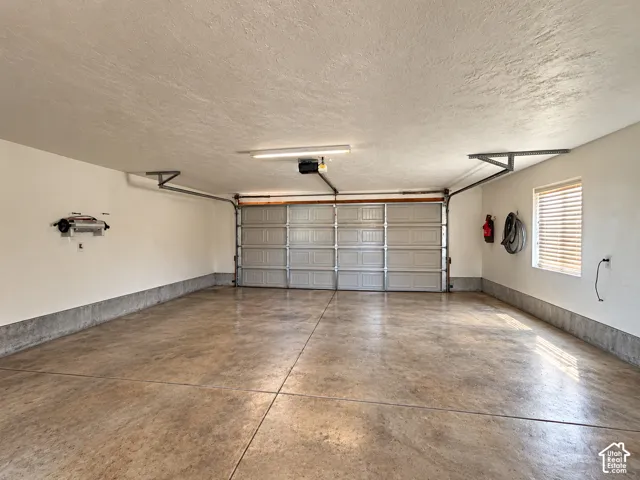 Multi-car garage featuring a concrete floor, painted walls, overhead lighting, and a window with blinds