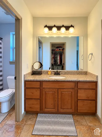 Wood-finish cabinetry with multiple drawers, stone-patterned countertop, integrated oval basin, and four-light wall-mounted fixture
