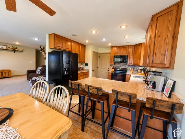 Kitchen featuring wood cabinetry, stone-finish countertops, tile flooring, recessed lighting, and a built-in breakfast bar