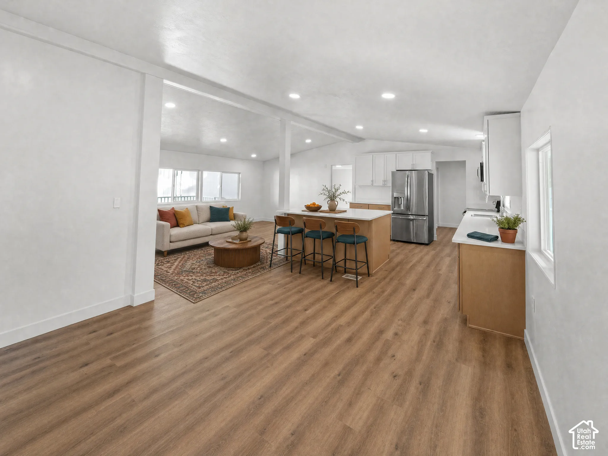 Open-concept interior featuring wood-finish flooring, recessed lighting, a central island with bar seating, and stainless steel kitchen appliances