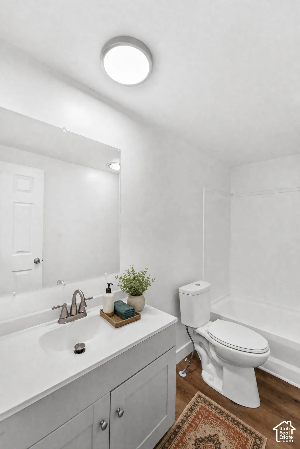 Vanity featuring a solid surface countertop, undermount sink, and metallic faucet, paired with a large wall-mounted mirror, overhead flush-mount lighting, and wood-finish flooring