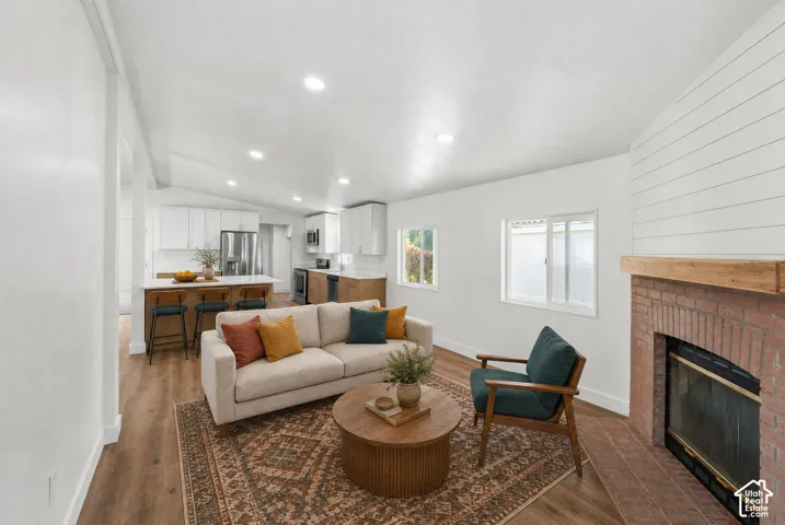 Vaulted ceiling with recessed lighting, wood-finish flooring, brick fireplace with a wood mantel, and shiplap wall detailing