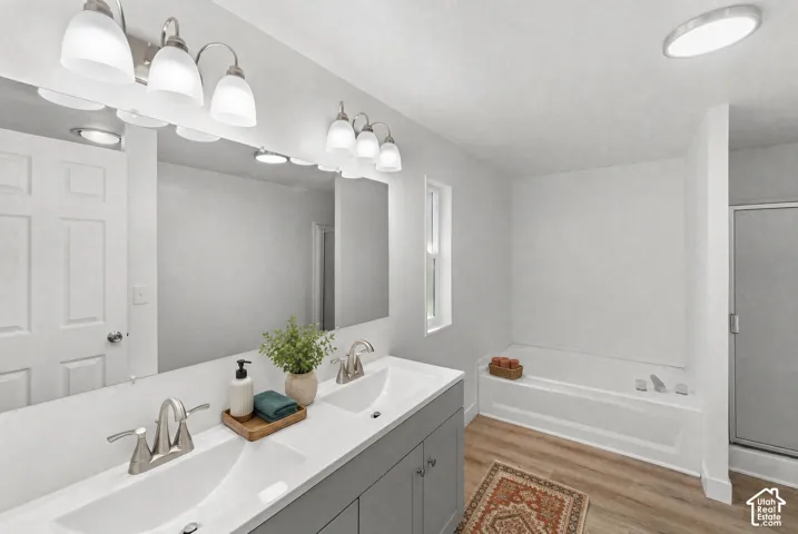 Dual-sink vanity with white countertops, expansive wall mirror, brushed metal hardware, soaking tub, and enclosed glass shower