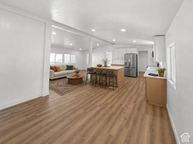 Open-concept interior featuring wood-finish flooring, recessed lighting, a central island with bar seating, and stainless steel kitchen appliances