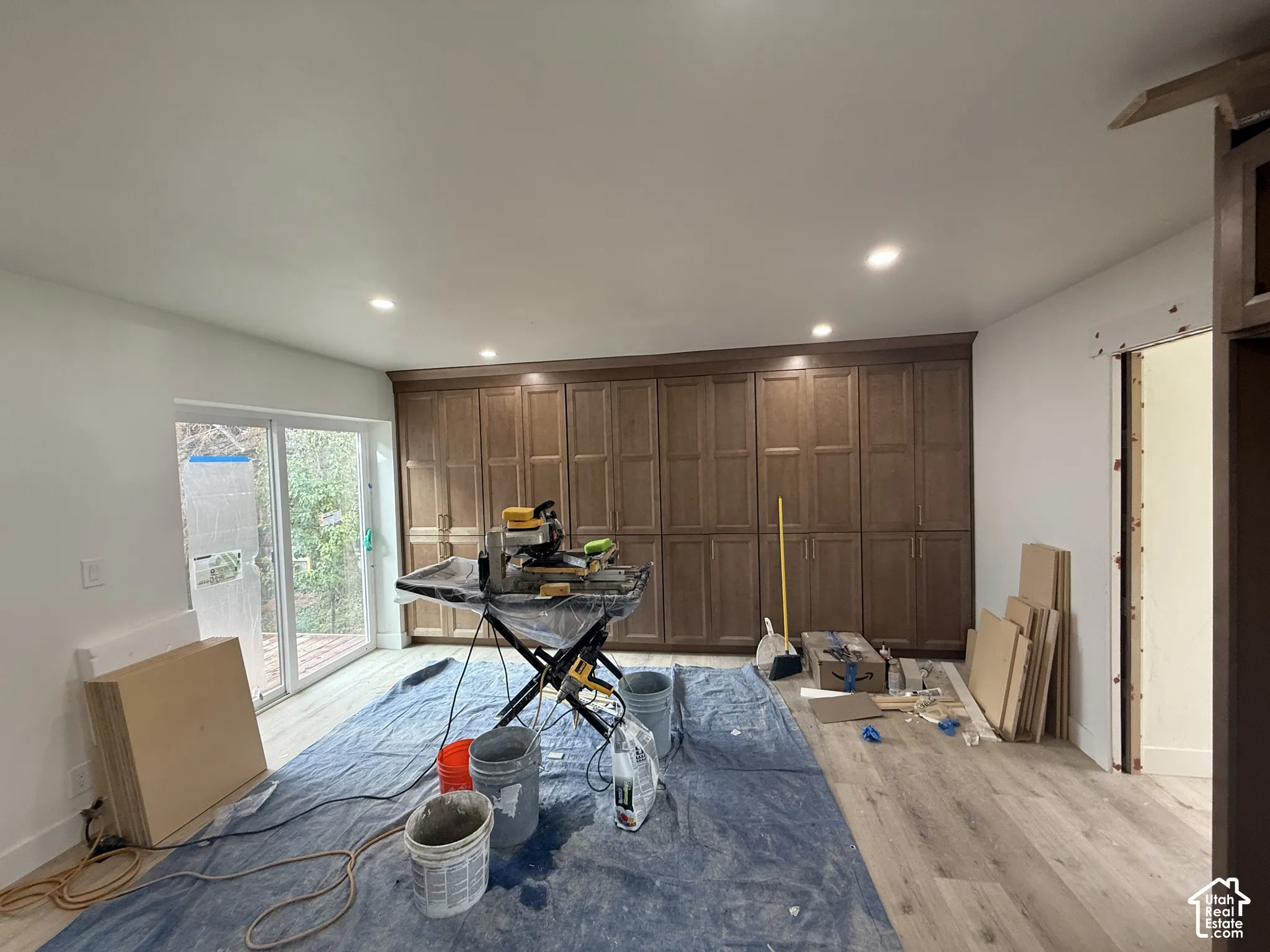Wall-to-wall built-in cabinetry with recessed panel doors, wood-finish flooring, recessed ceiling lighting, and sliding glass door