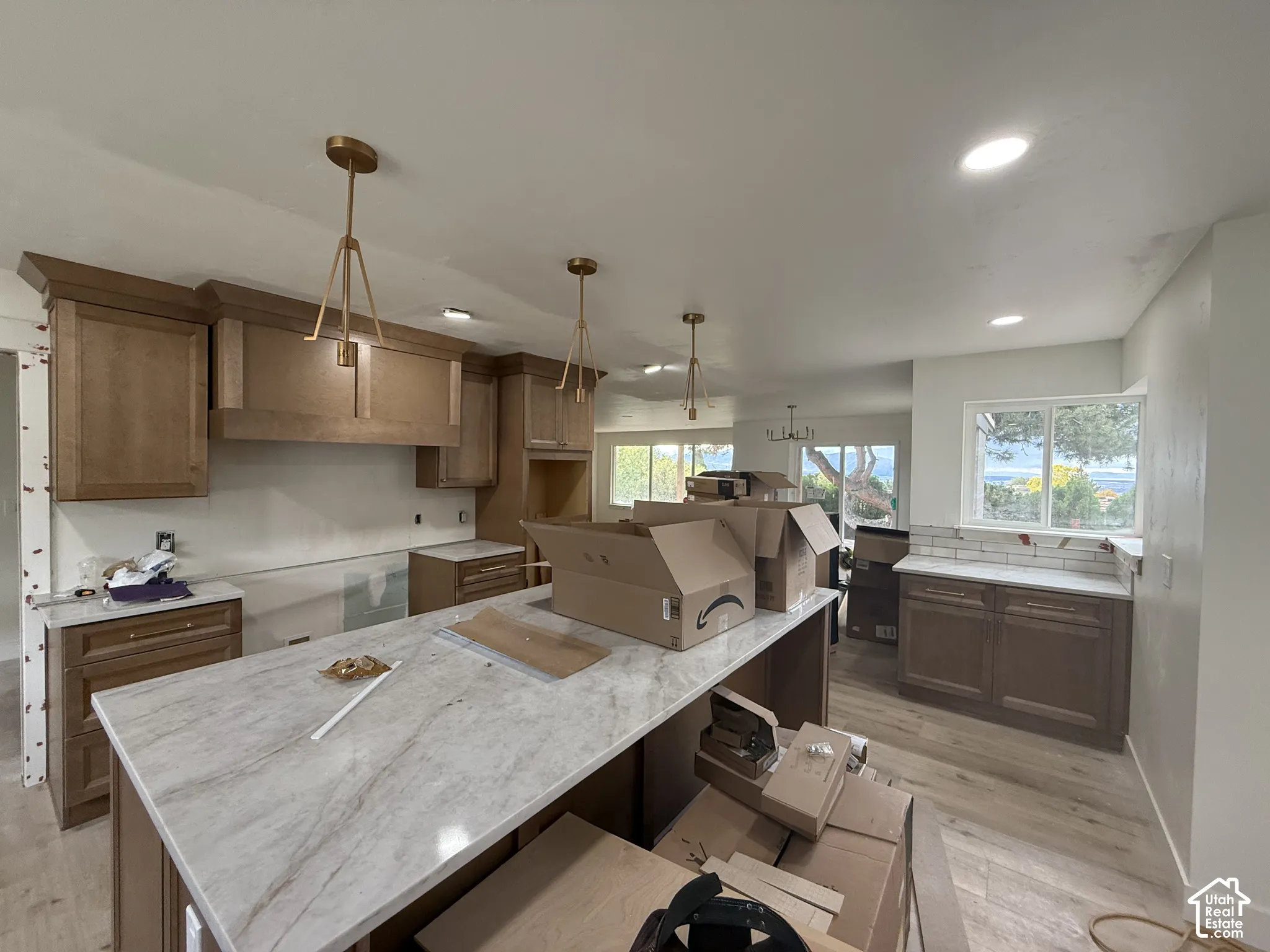 Kitchen featuring wood-finish cabinetry, an expansive center island with a stone-patterned countertop, gold-finish pendant lighting, and wood-finish flooring