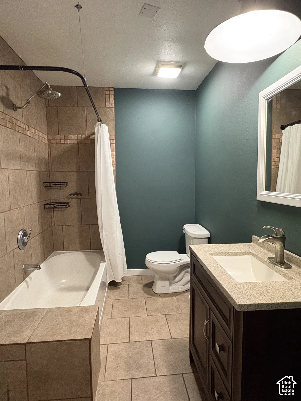 Bathroom featuring tiled tub surround with mosaic accent, dark wood-finish vanity with integrated solid surface countertop, tile flooring, and wall-mounted light fixtures