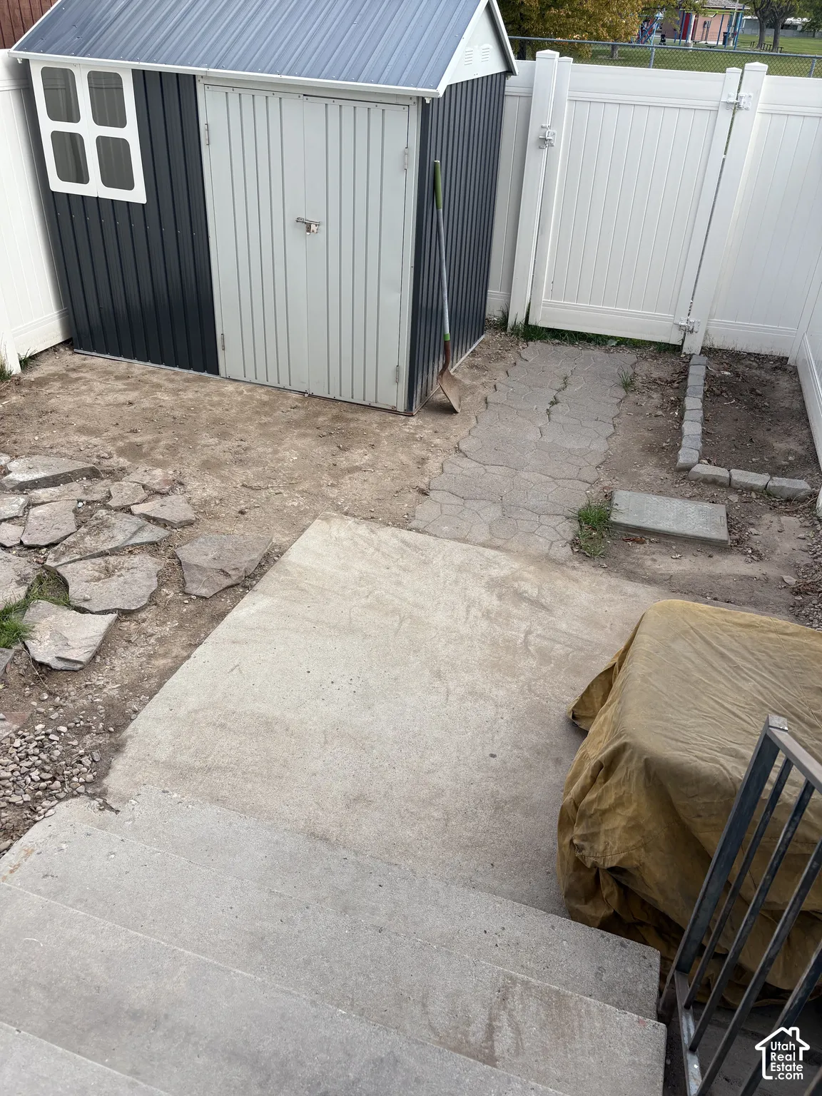 Exterior area featuring a metal storage structure, vinyl privacy fencing, concrete patio, and stone paver pathways