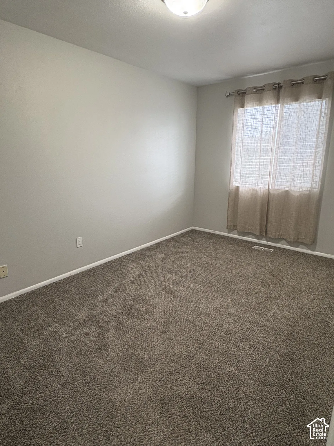 Neutral-toned room featuring wall-to-wall carpeting and a single window with an installed metal curtain rod