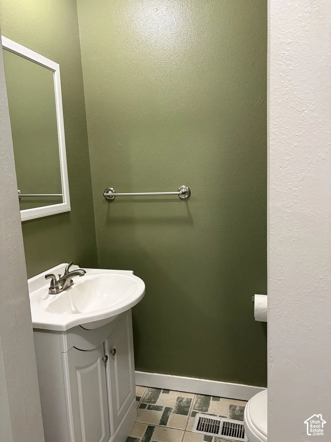 White vanity cabinet with an integrated white sink, brushed nickel faucet, wall-mounted mirror with a white frame, and tiled flooring