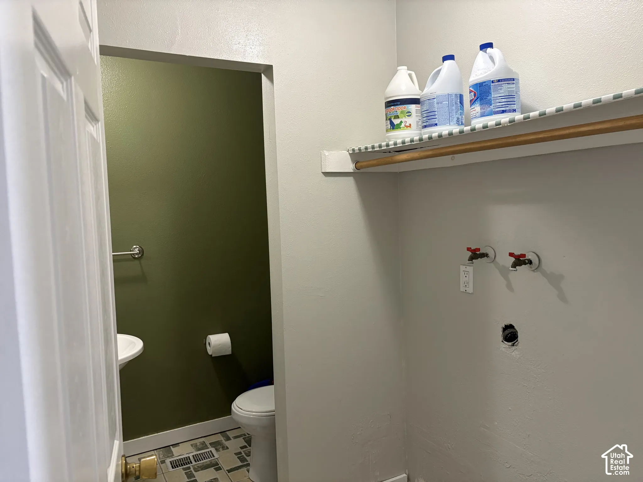 Laundry utility area featuring a wall-mounted shelving unit with a wooden hanging rod, standard water hookups, and patterned tile flooring