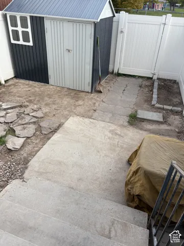 Exterior area featuring a metal storage structure, vinyl privacy fencing, concrete patio, and stone paver pathways