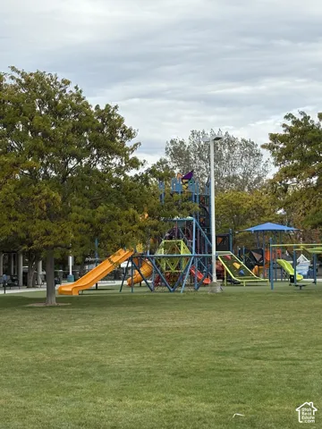Outdoor recreational space featuring a multi-level playground structure, integrated slides, a climbing frame, and mature trees situated on a level grass area