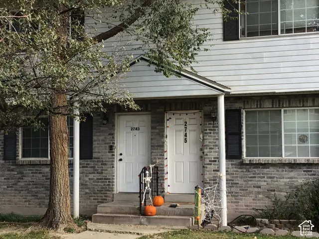 Multi-unit exterior featuring gray brick lower facade, horizontal siding, shuttered windows, and a covered entryway with a gabled roof