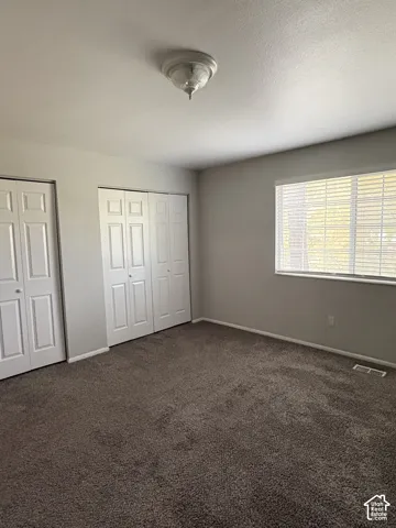 Neutral-toned interior featuring wall-to-wall carpeting, dual bifold closet doors, and large windows with horizontal blinds