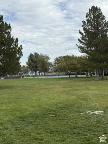 Expansive lawn area featuring mature pine and deciduous trees with a fenced tennis court