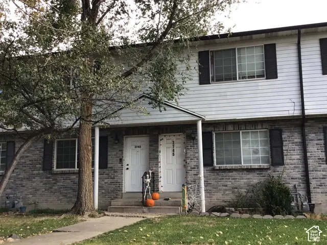 Two-story townhome exterior featuring gray brick masonry lower level, white horizontal siding upper level, and dark window shutters
